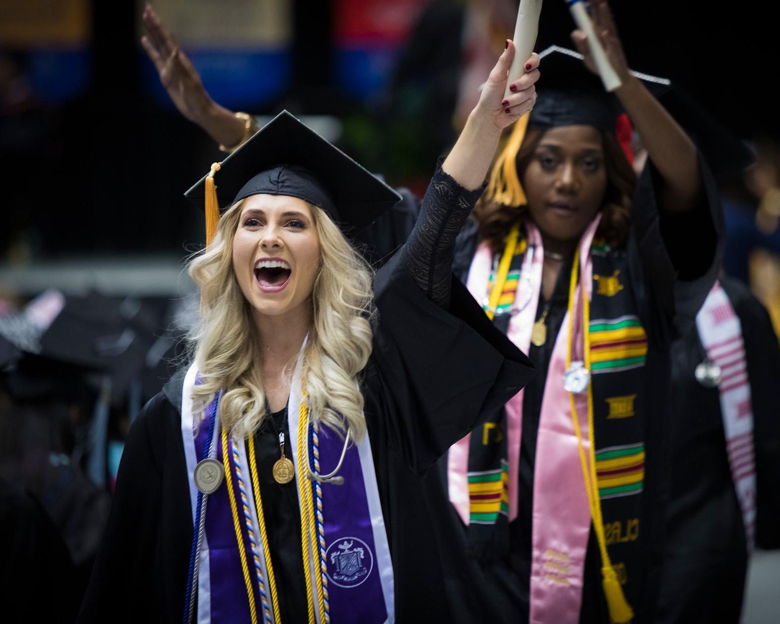 两个女人(一个白人，一个非裔美国人)拿着毕业证书走在路上